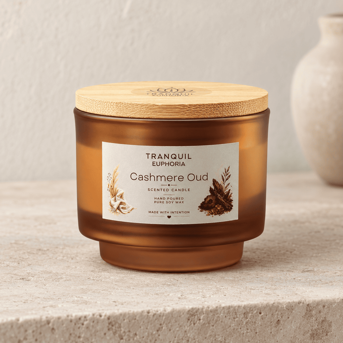 A Tranquil Euphoria 'Cashmere Oud' scented candle in an amber glass jar with a light bamboo lid, set on a textured stone surface with a neutral background.