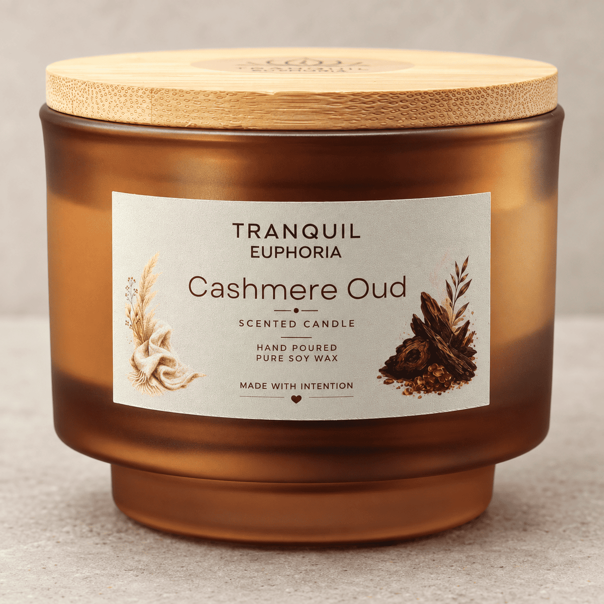 A Tranquil Euphoria 'Cashmere Oud' scented candle in a frosted amber glass jar with a light bamboo lid, shown on a neutral textured background.