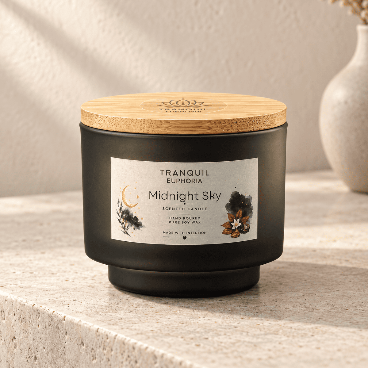 A Tranquil Euphoria 'Midnight Sky' scented candle in a matte black jar with a light bamboo lid, set on a textured beige stone surface with a neutral background.