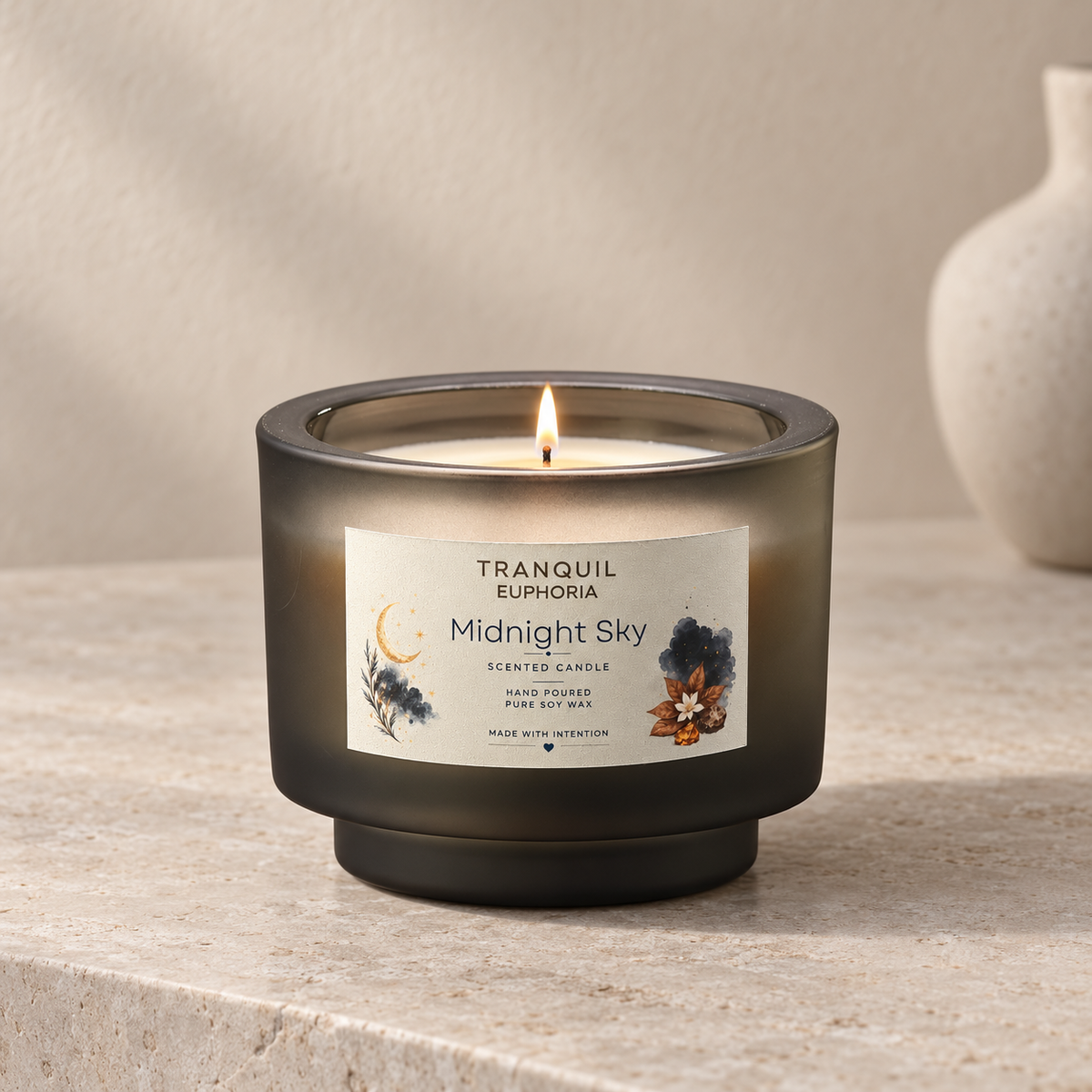 A lit Tranquil Euphoria 'Midnight Sky' scented candle in a dark smoky glass jar, set on a textured stone surface with a neutral background and a ceramic vase in the distance.