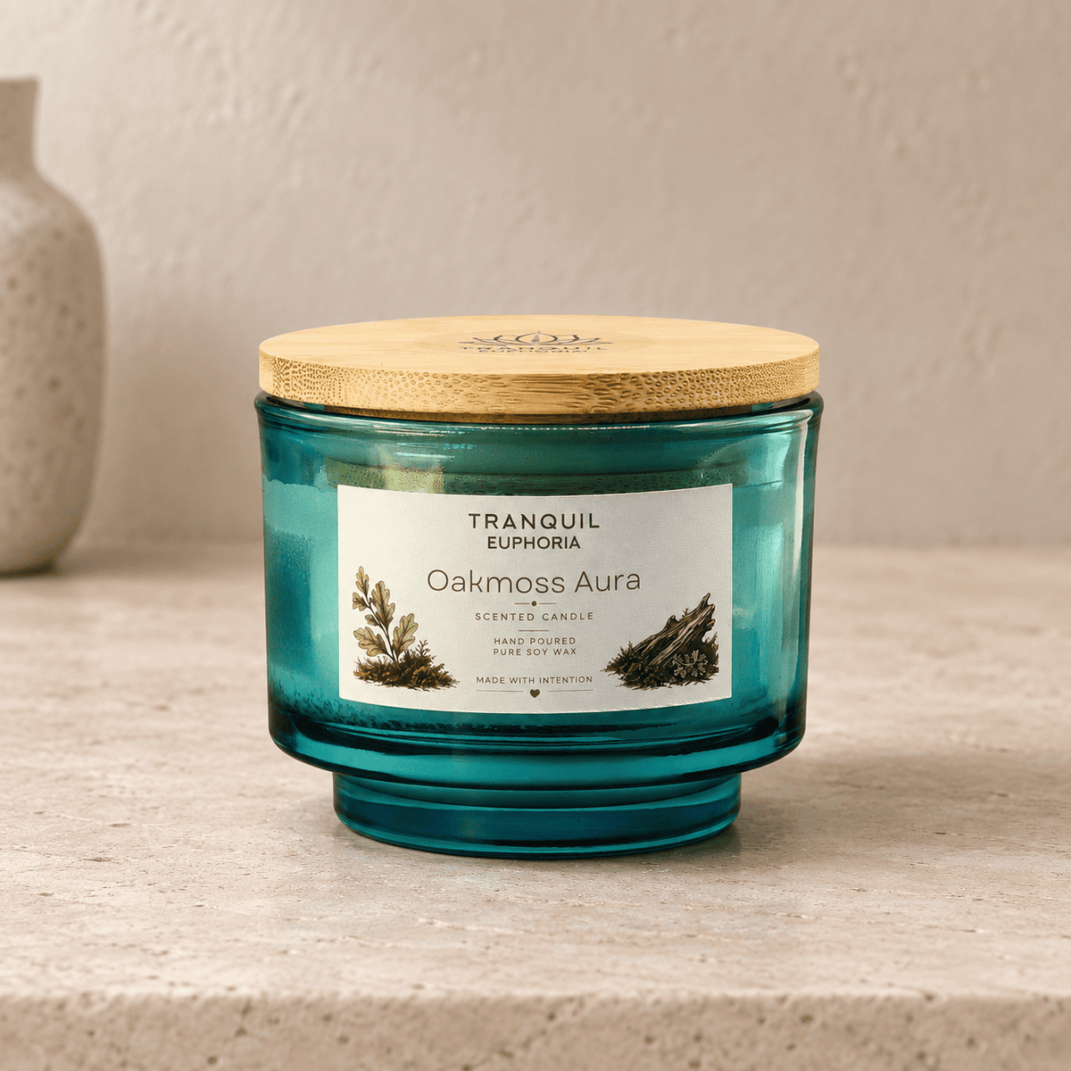 A teal-blue glass scented candle jar with a light wood lid sits on a beige stone surface against a textured beige wall. The front label reads 'TRANQUIL EUPHORIA' and 'Oakmoss Aura'.