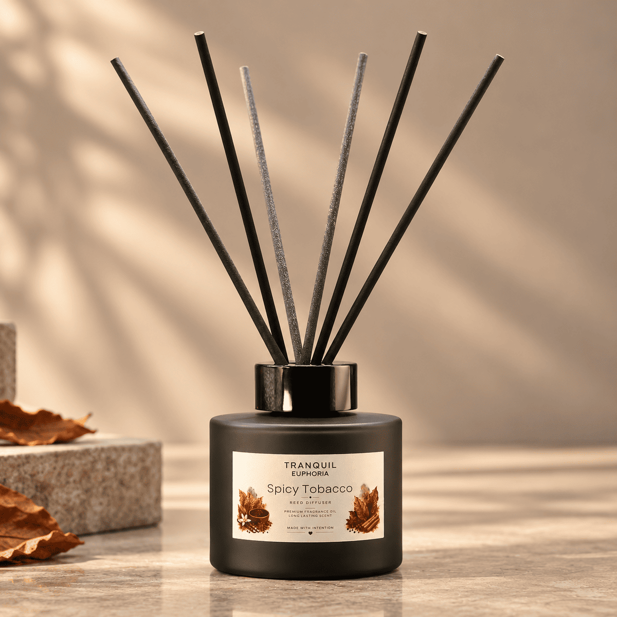 A reed diffuser bottle with six black reeds, labeled 'Tranquil Euphoria Spicy Tobacco', set on a stone surface with warm shadows and dried leaves in the background.