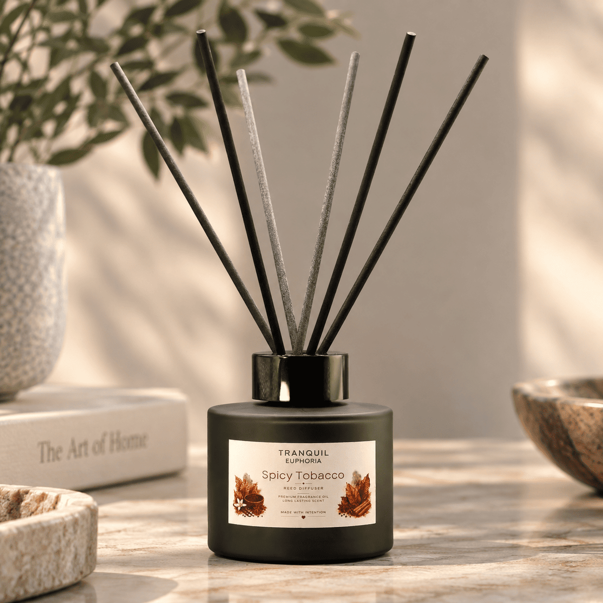 A reed diffuser bottle labeled Tranquil Euphoria Spicy Tobacco, with black reeds and a black glass bottle, set on a wooden table with a warm neutral background.