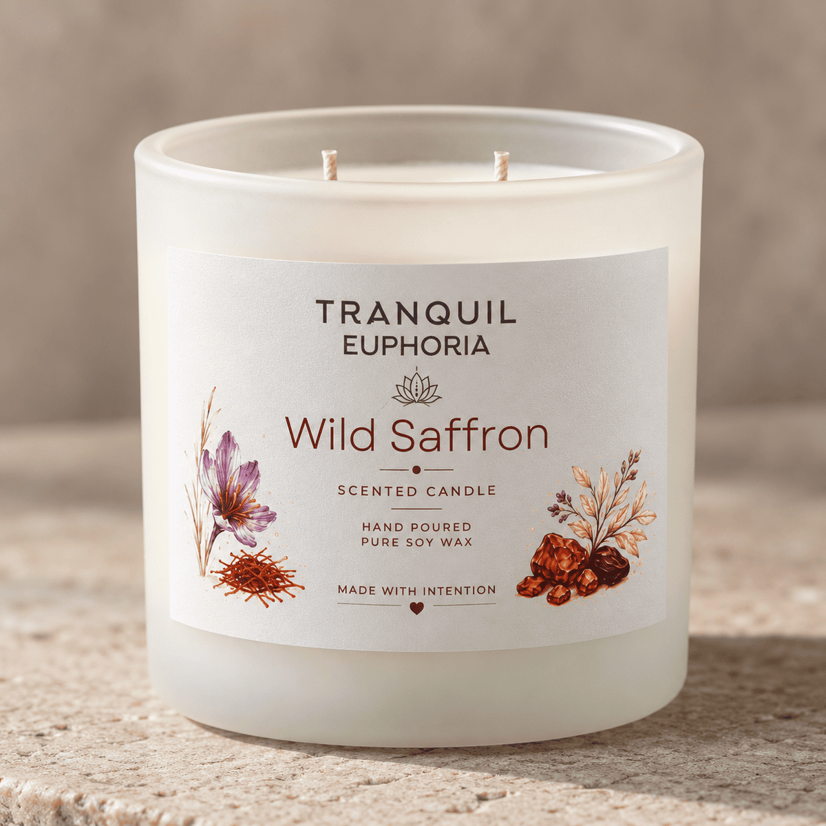 A frosted glass scented candle labeled 'Tranquil Euphoria Wild Saffron' with two wicks, shown on a textured beige stone surface against a neutral beige background.